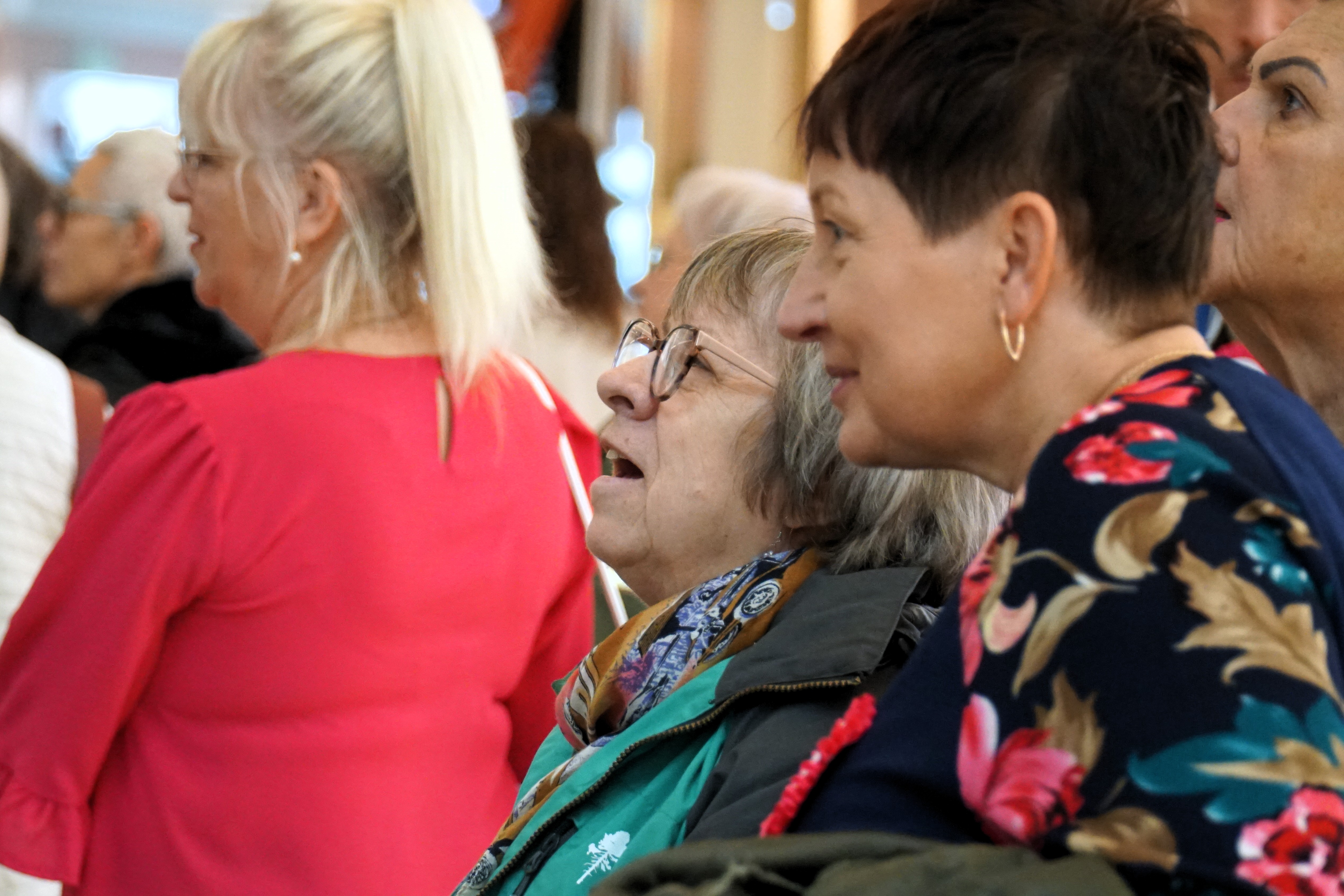 Zbliżenie na uczestniczki wystawy przyglądające się zdjęciom dokumentującym projekt Oddech dla Mam. W tle fragment galerii Posnania.